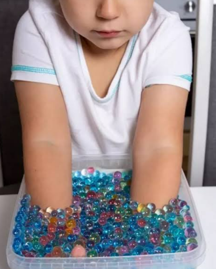 Child engaging in sensory integration with colorful water beads